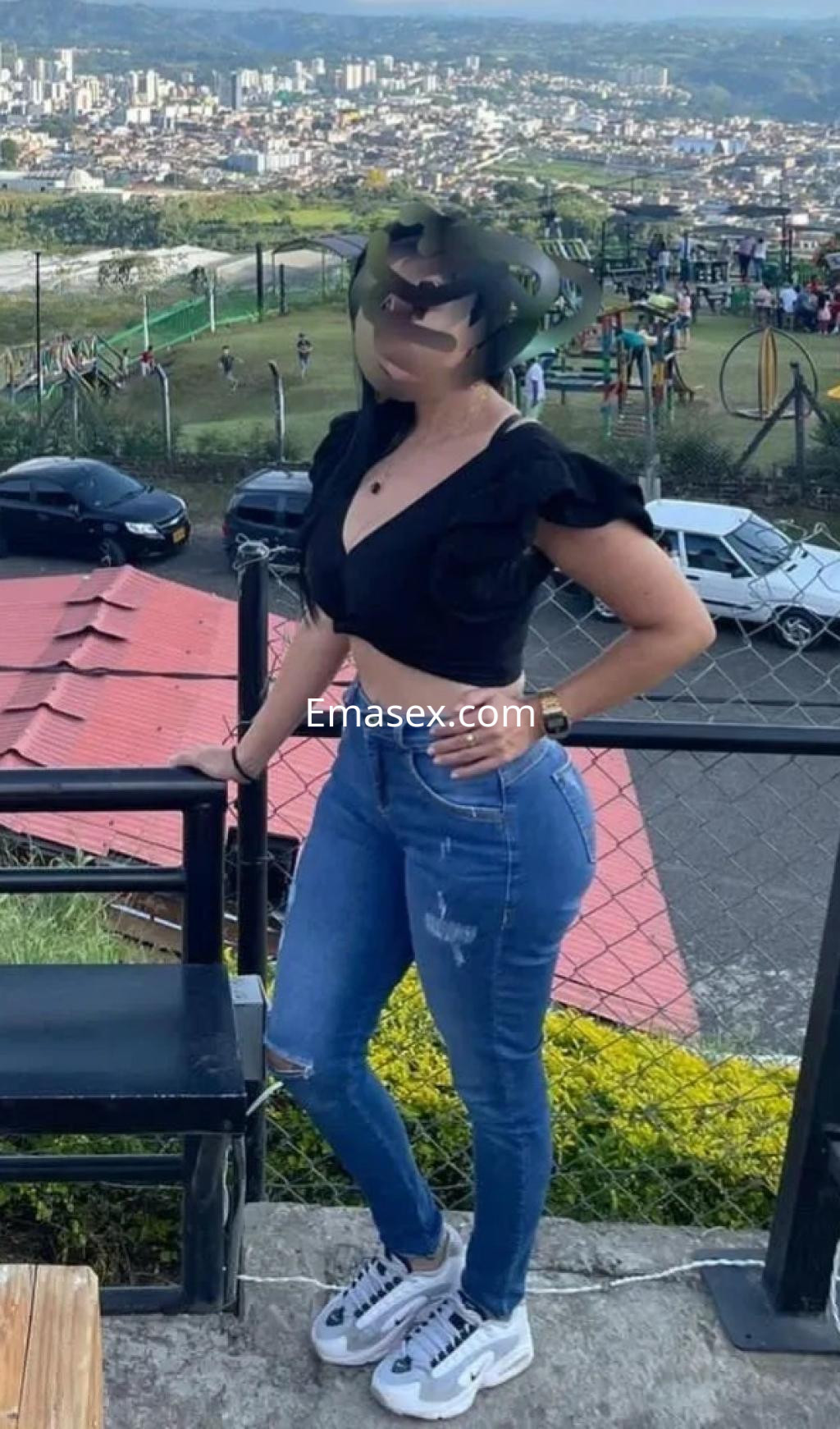 Puta con blusa negra y jeans ajustados, posando en un entorno al aire libre en Oviedo.