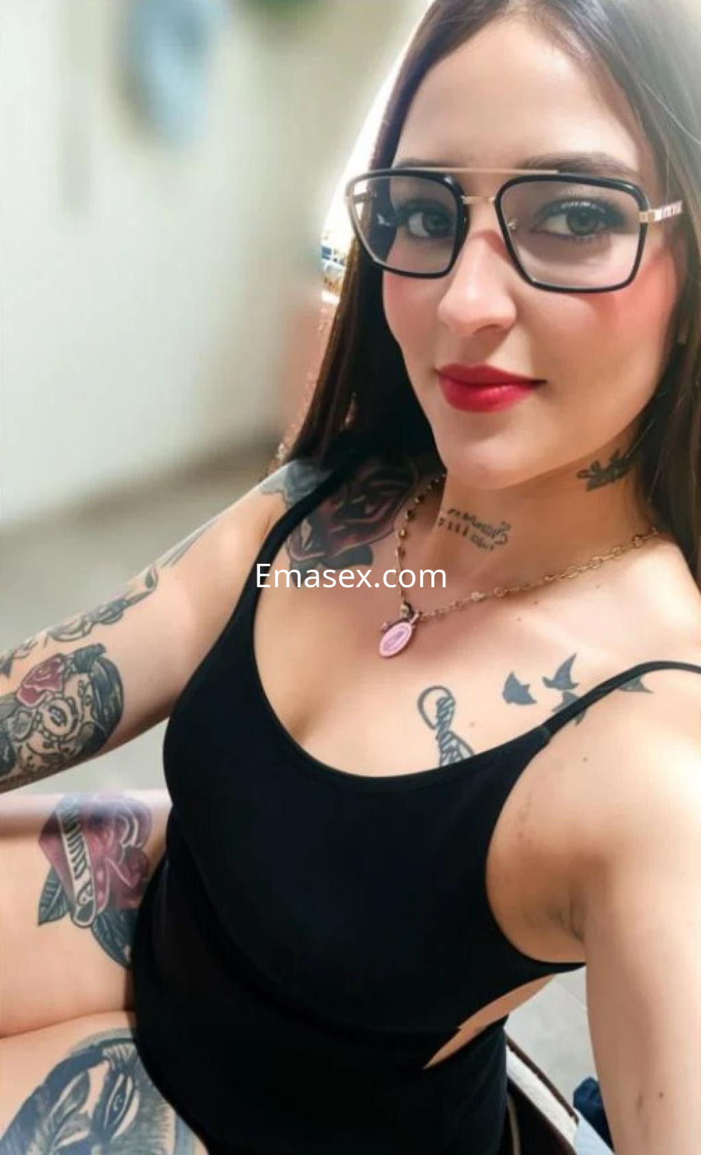 Puta en Oviedo con cabello largo y lacio, usando gafas y un body negro, mostrando tatuajes en brazos y pecho.