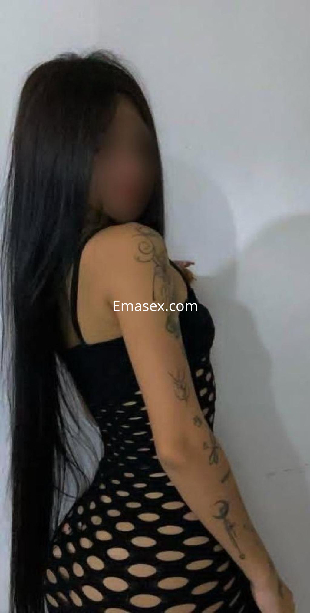 Puta en Valladolid, luciendo un vestido negro de malla con patrones circulares y tatuajes visibles en el brazo.