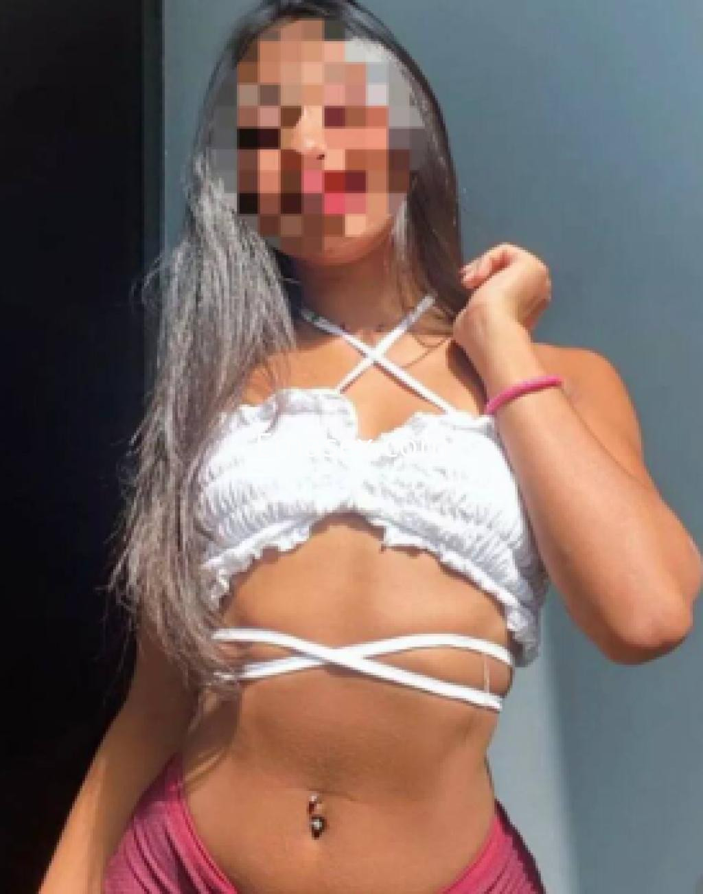 Puta en Logroño luciendo un top blanco con tiras decorativas y una falda corta roja, posando con confianza.