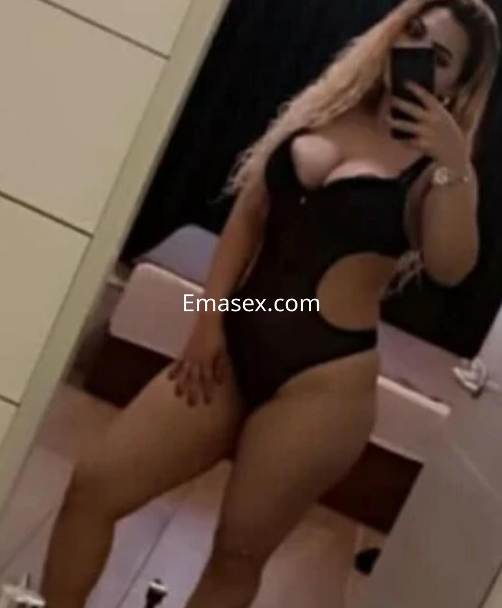 Escort en Oviedo posando en un espejo con un body negro que resalta su figura y cabello largo.