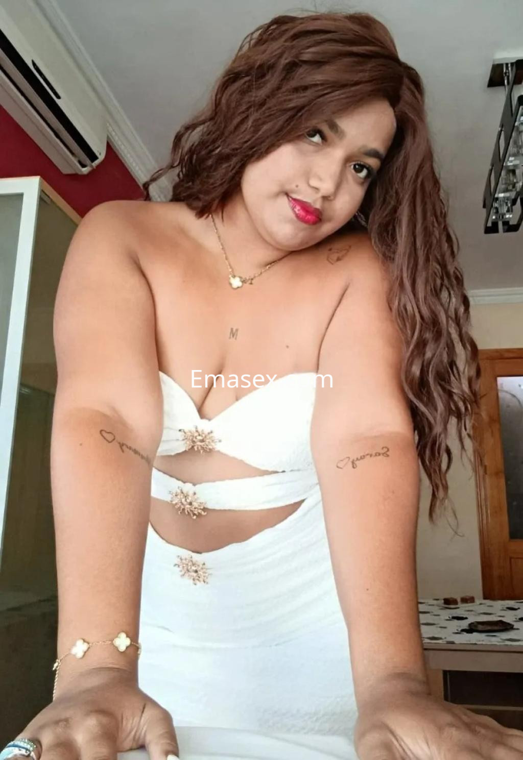 Escort en Málaga con vestido blanco ajustado, cabello largo y rizado, posando con una expresión seductora.
