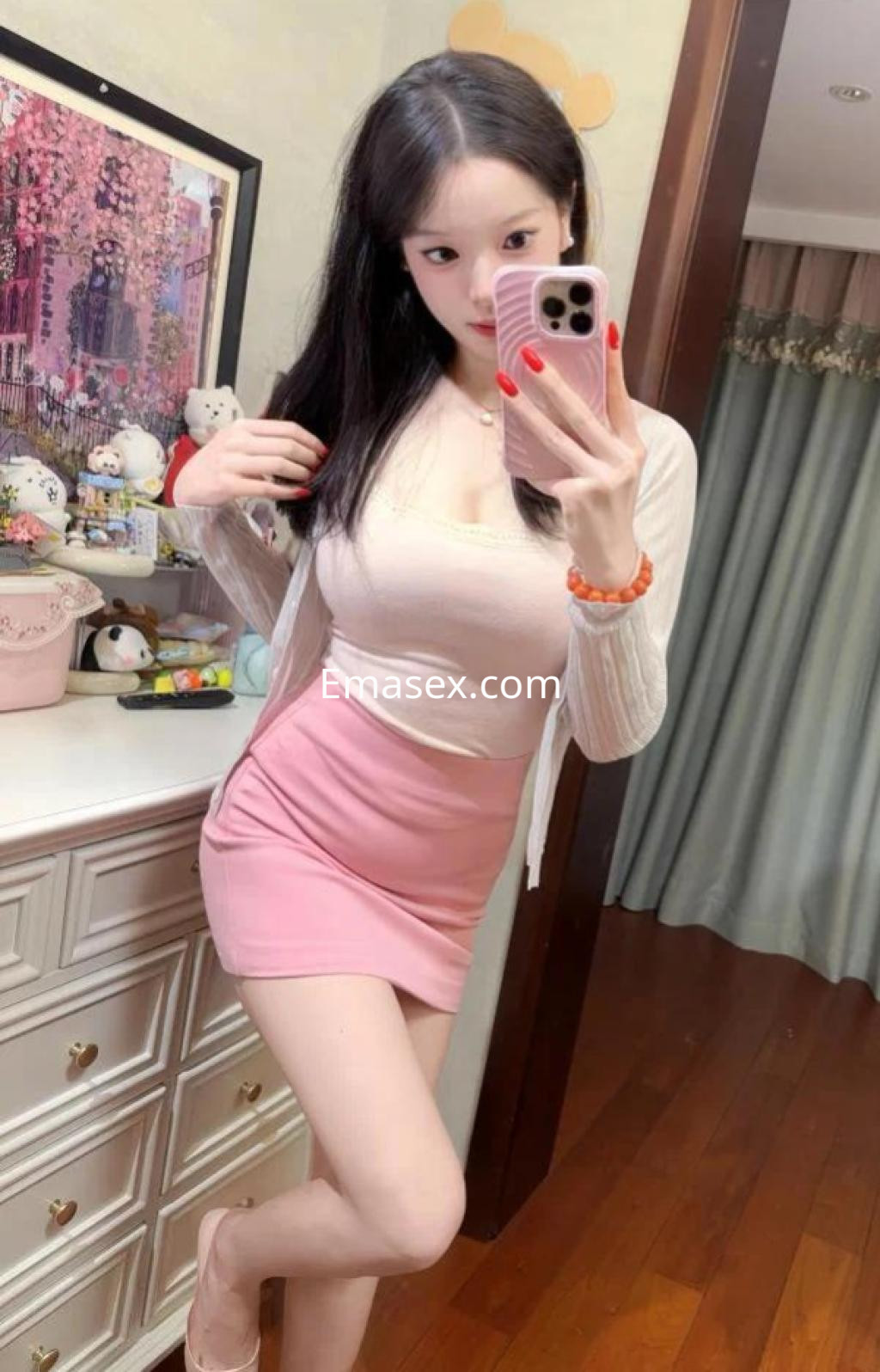 Puta en Málaga, posando con un vestido rosa corto y un suéter blanco, en un entorno interior decorado.