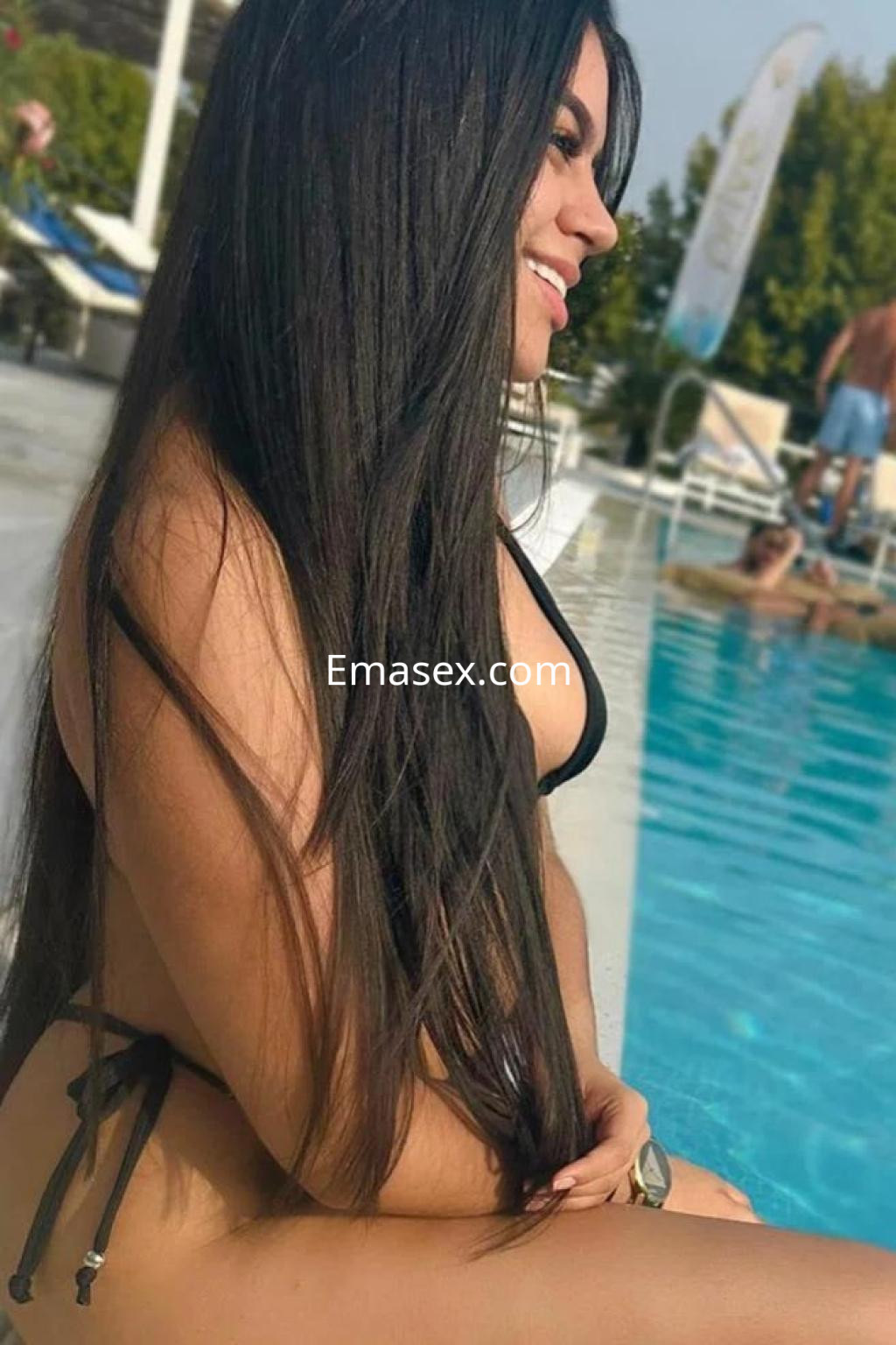 Puta en Málaga con cabello largo y lacio, luciendo un bikini negro junto a la piscina, sonriendo.