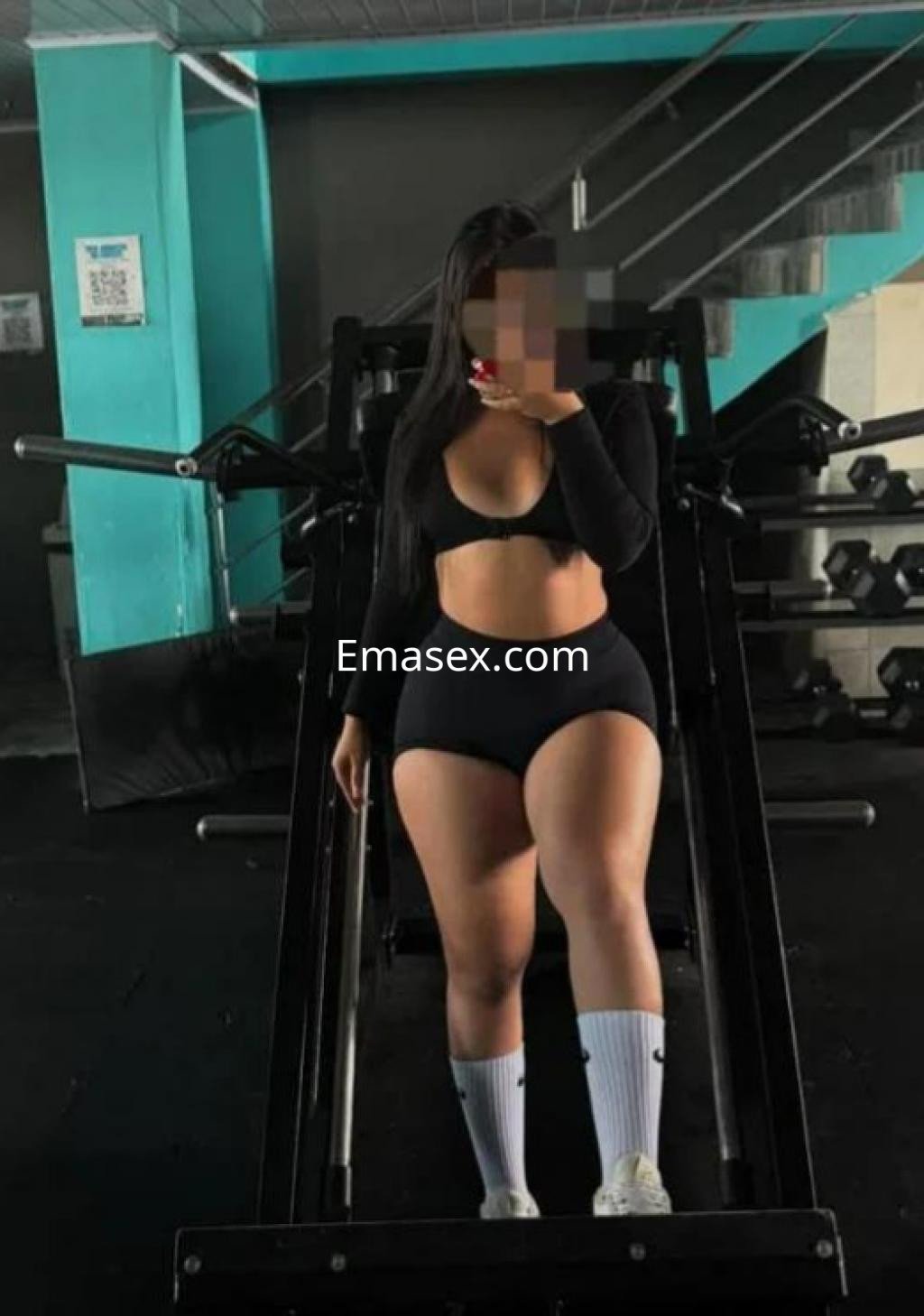 Puta en Las Palmas posando en un gimnasio, vistiendo un top negro y shorts, con calcetas deportivas blancas.