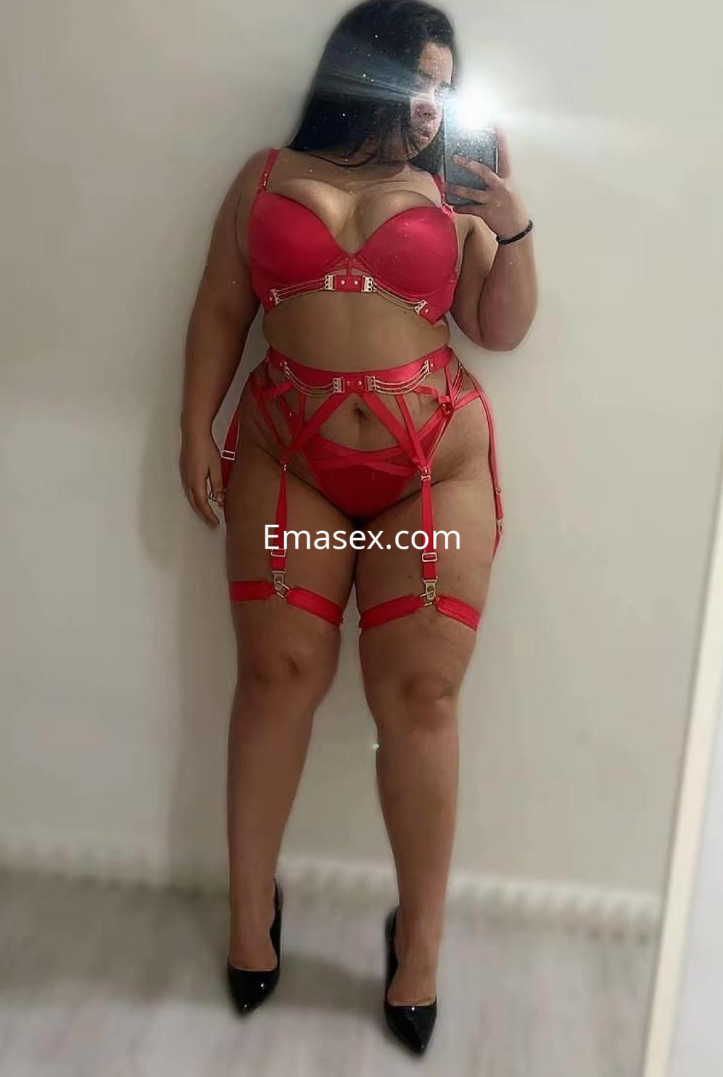 La escort se muestra en Santander con un conjunto de lencería roja que resalta su figura y tacones negros.