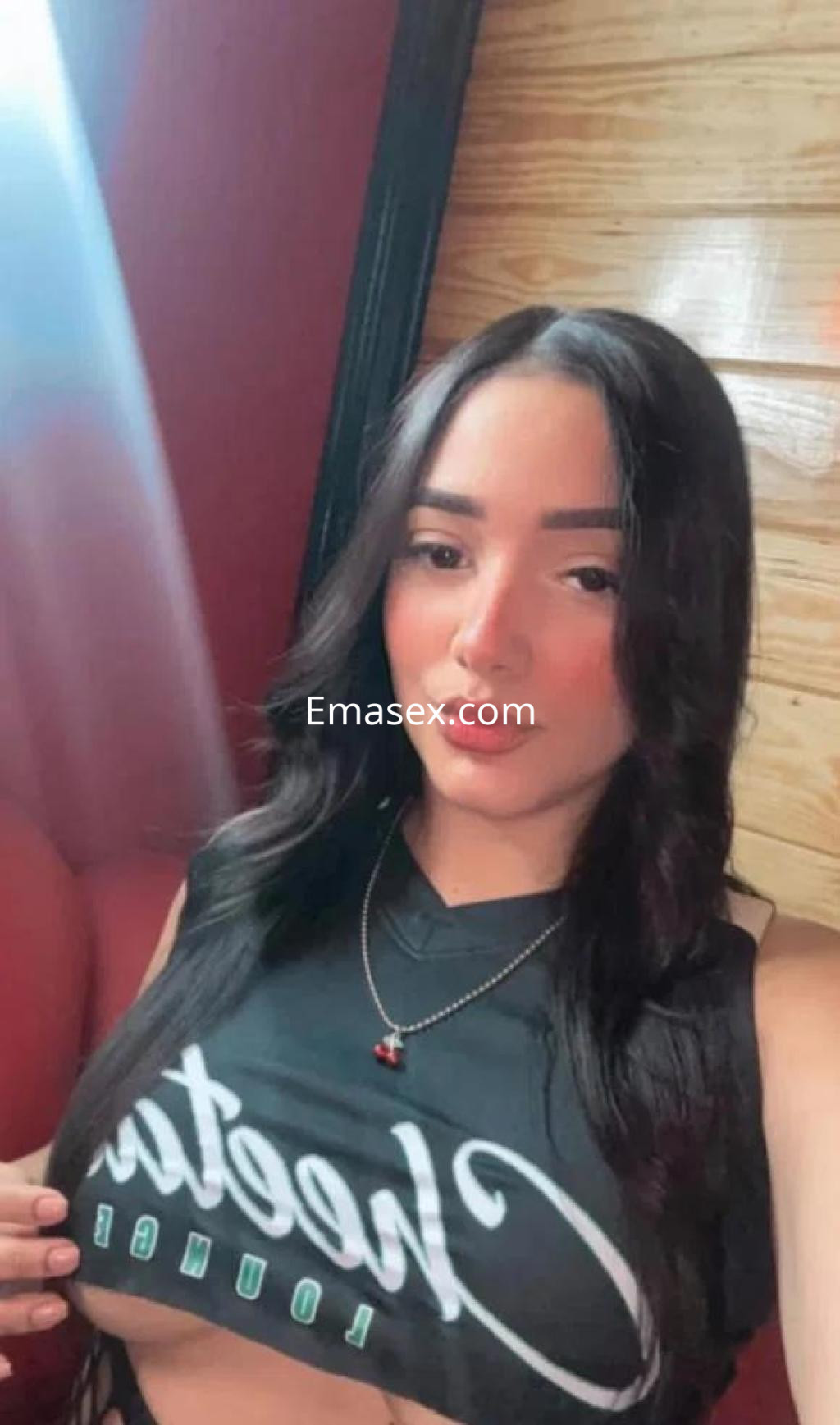 La puta en Almería posa en un ambiente interior con una camiseta negra, mostrando una sonrisa y cabello largo.