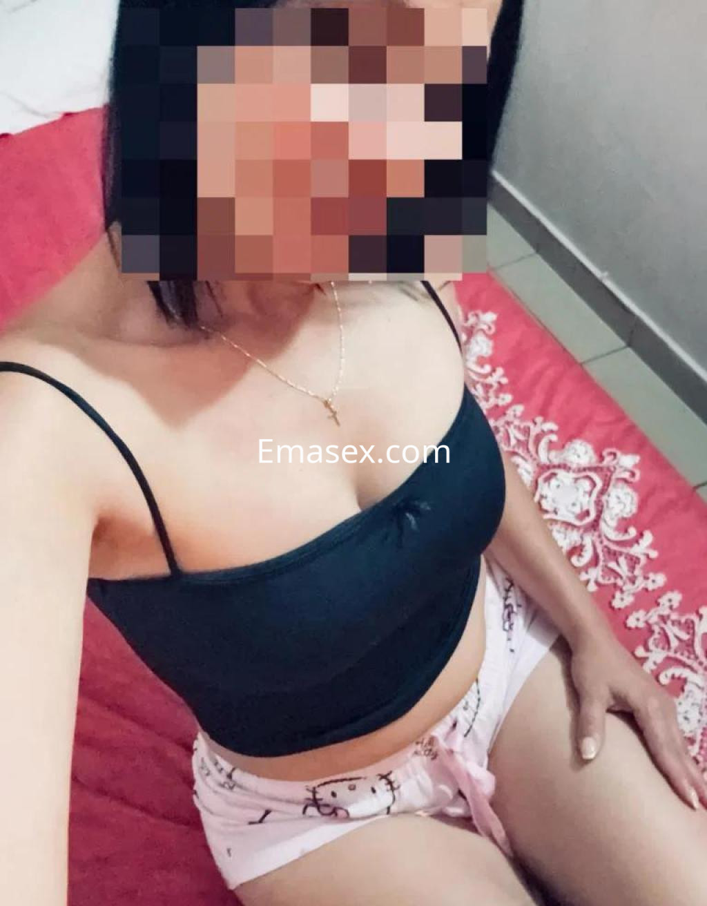 Puta sentada en una cama con sábanas rojas, vistiendo una blusa sin mangas negra y pantalones cortos claros en Tenerife.