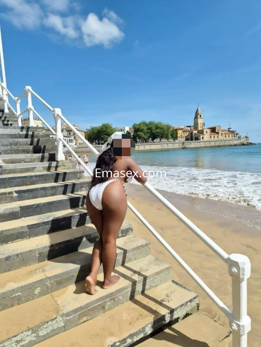 Puta en la playa de Oviedo, luciendo un bikini blanco mientras se apoya en las escaleras junto al mar.