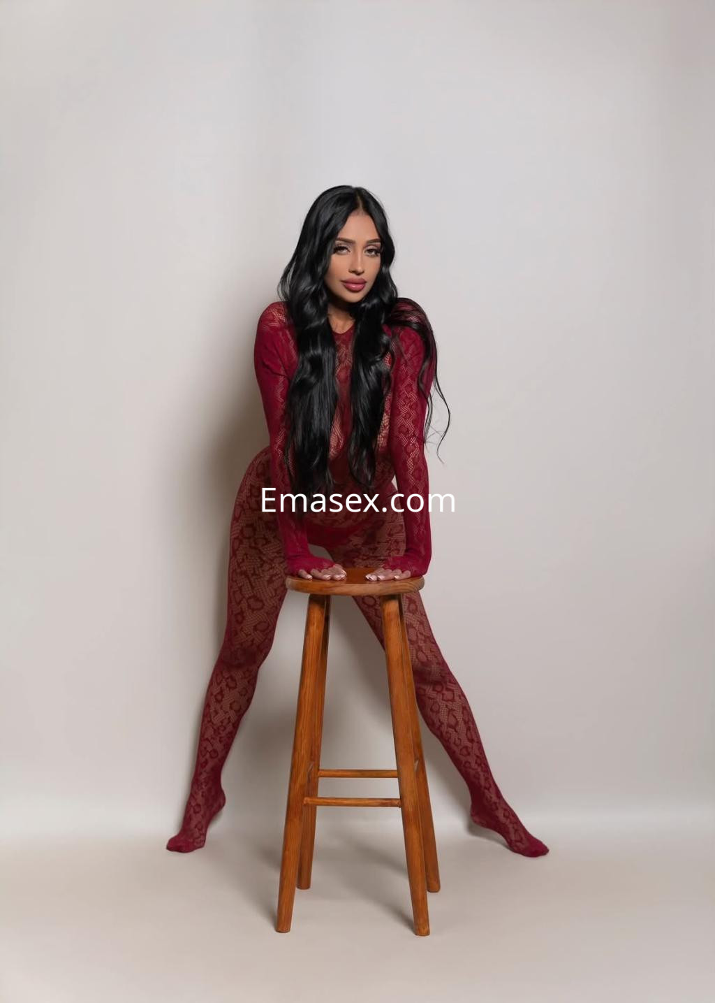 La puta posa de manera seductora con mallas rojas transparentes y cabello largo en un fondo neutro en Murcia.