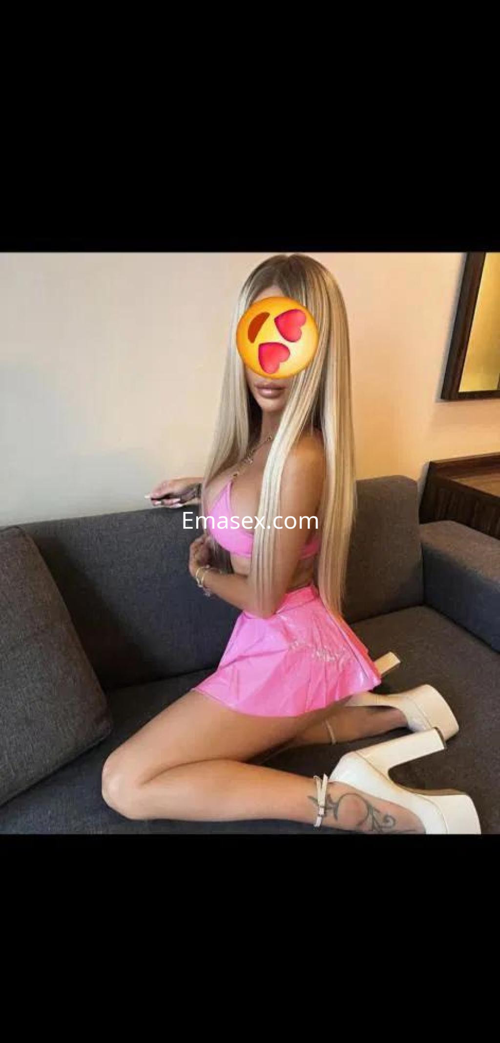 Escort en Almería con cabello largo y lacio, vistiendo un vestido rosa y tacones, sentada en un sofá.