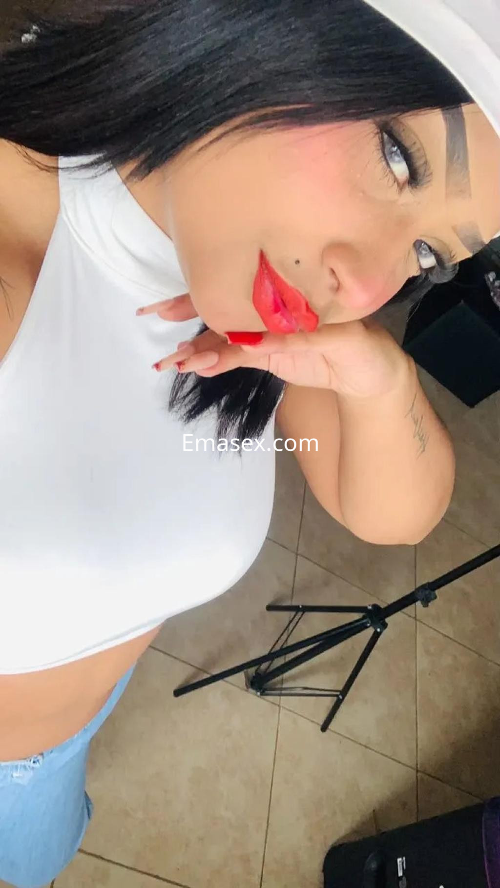 La puta en Granada luce una blusa blanca ajustada y jeans, con labios rojos y una mirada seductora.