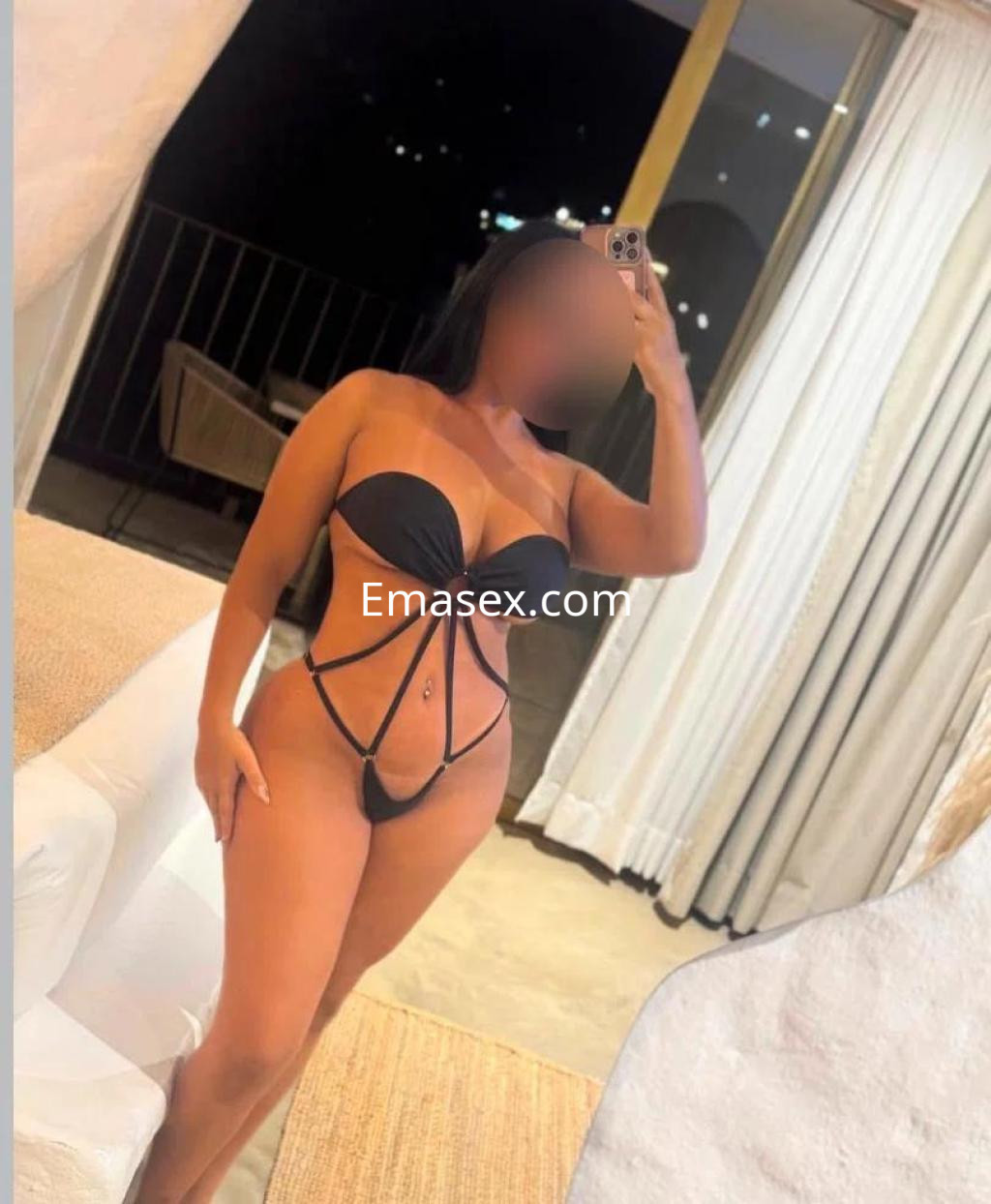 La escort en Tenerife posa con un bikini negro de diseño atrevido frente a un espejo en un entorno elegante.