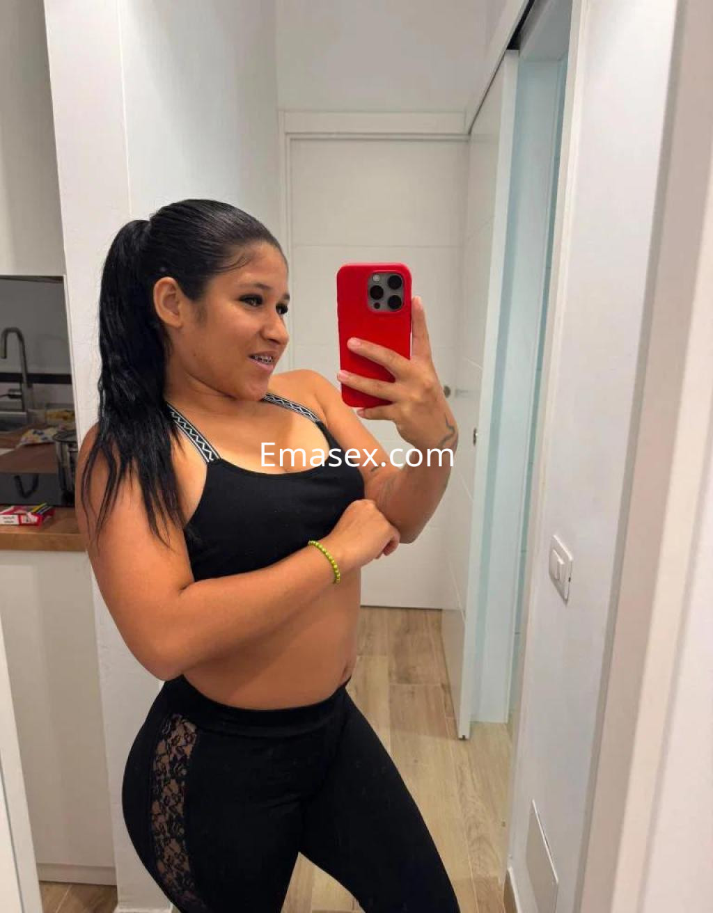 Escort en Tenerife, con cabello largo y oscuro, viste un top deportivo y mallas ajustadas, sonriendo en un espejo.