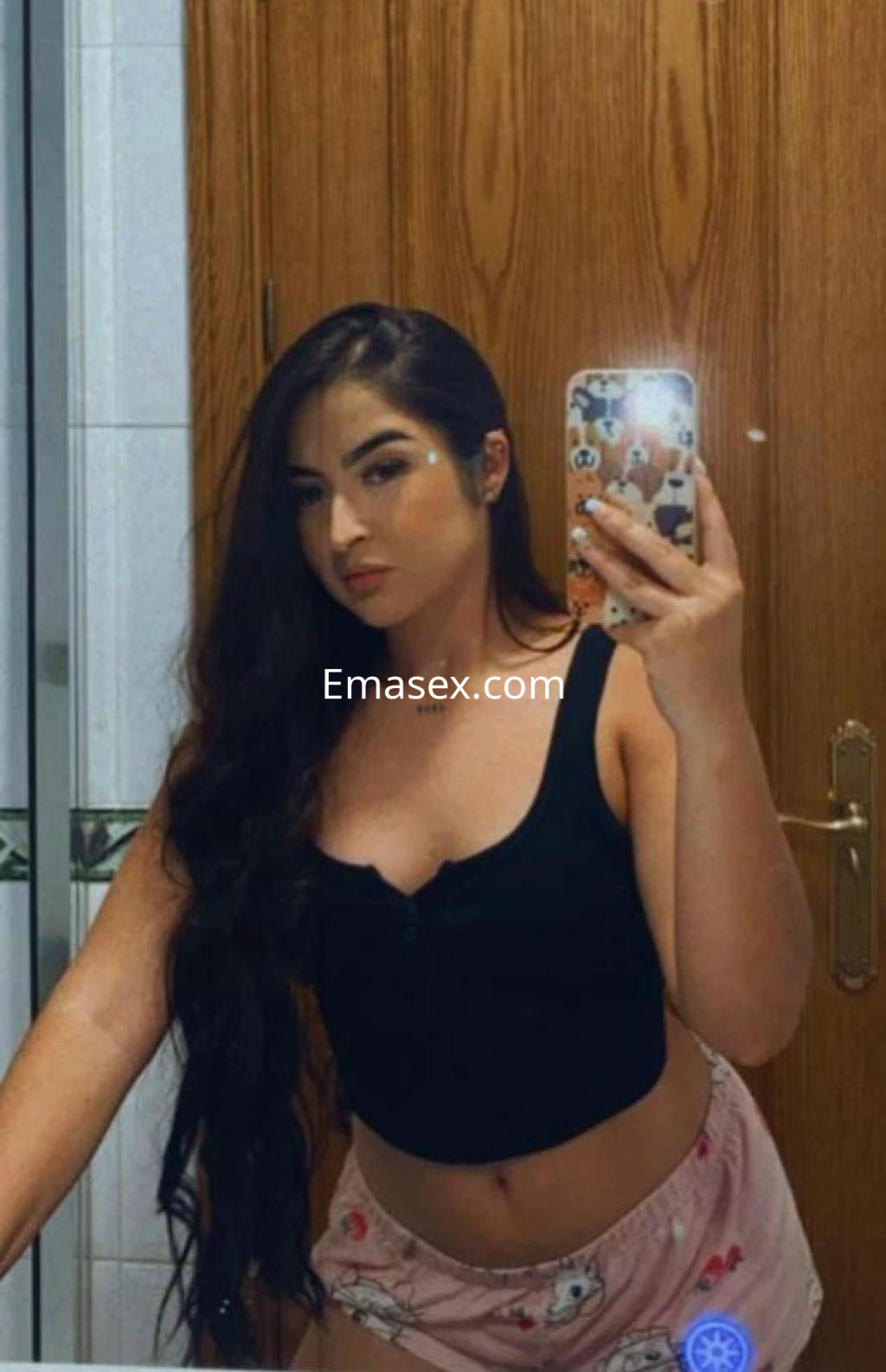 Puta con cabello largo y oscuro, viste una camiseta negra y pantalones cortos en un baño en Girona.