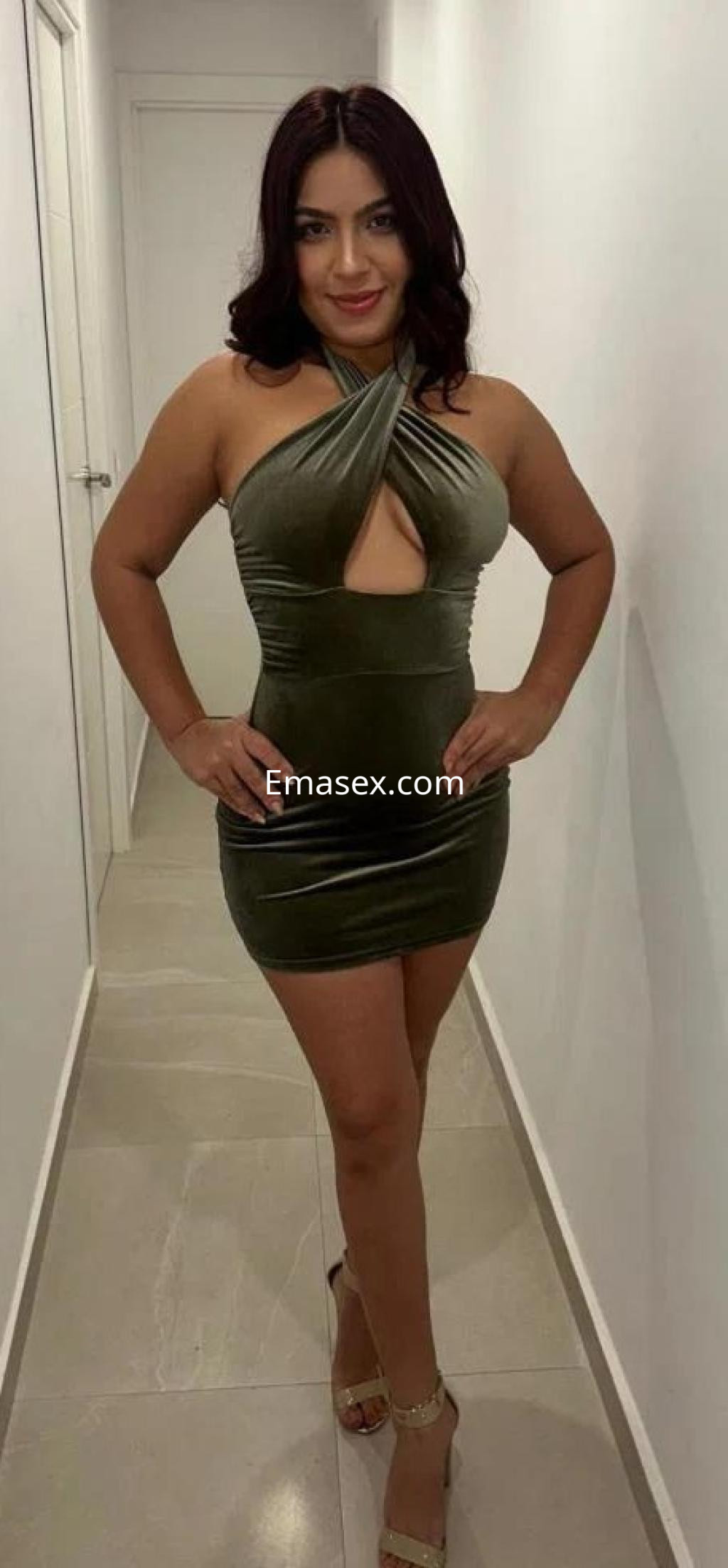 Escort en Málaga luciendo un vestido corto de terciopelo verde con escote y sandalias altas en un pasillo.