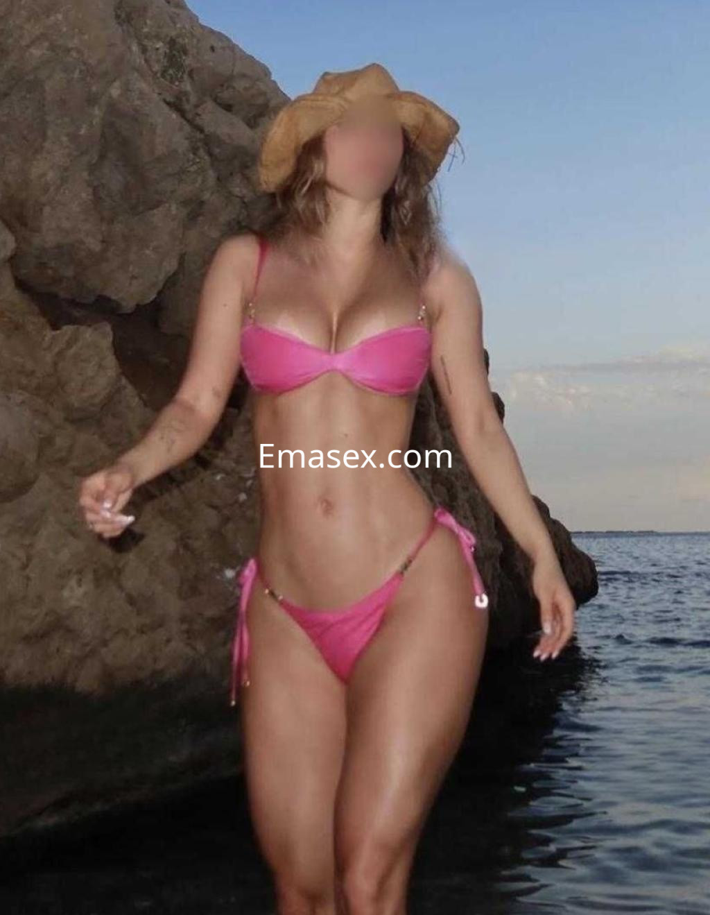 Puta en Logroño luciendo un bikini rosa y un sombrero, caminando cerca del agua y rocas.
