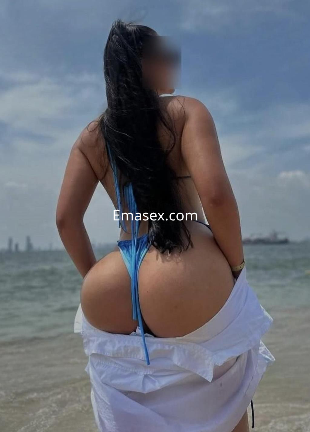 Puta posando de espaldas en la playa, luciendo un bikini azul y una camisa blanca abierta, con el mar de fondo en Logroño.