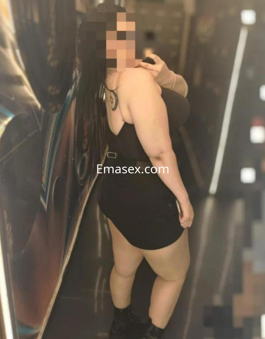 Escort en Madrid posando de perfil, lleva un vestido ajustado negro y botas, con cabello largo y oscuro.