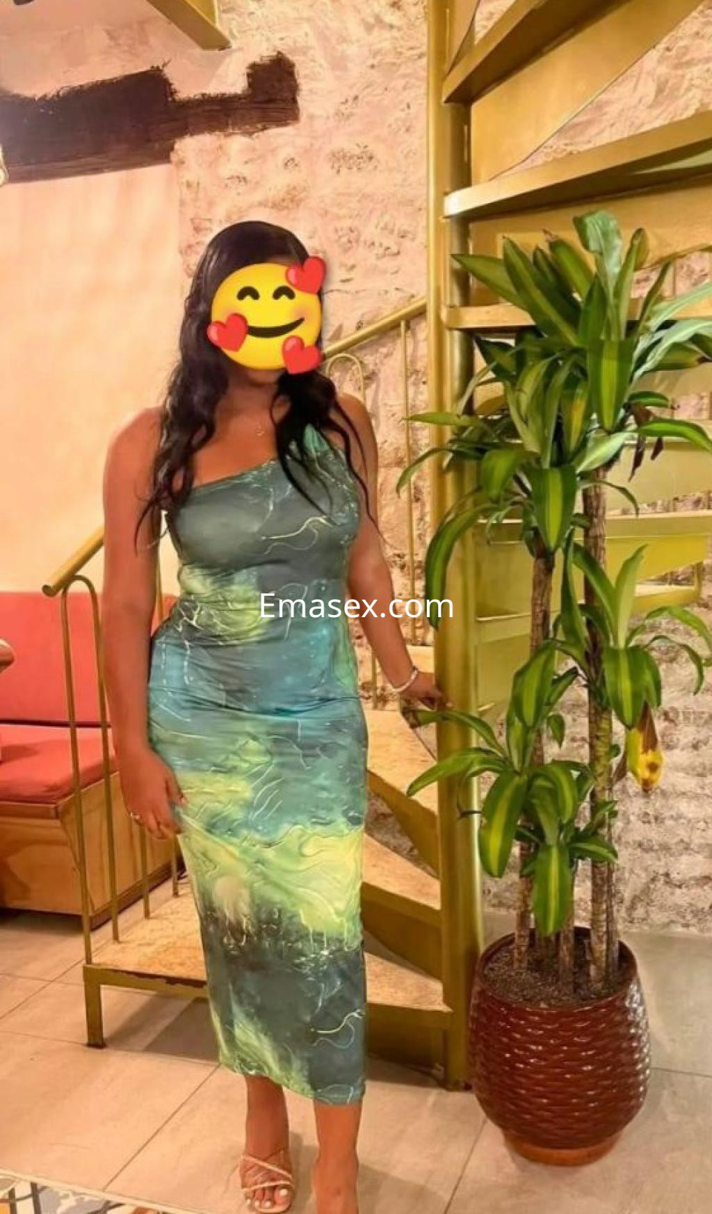Puta posando en Lleida con un vestido ajustado de tonos verdes y un fondo con plantas decorativas.