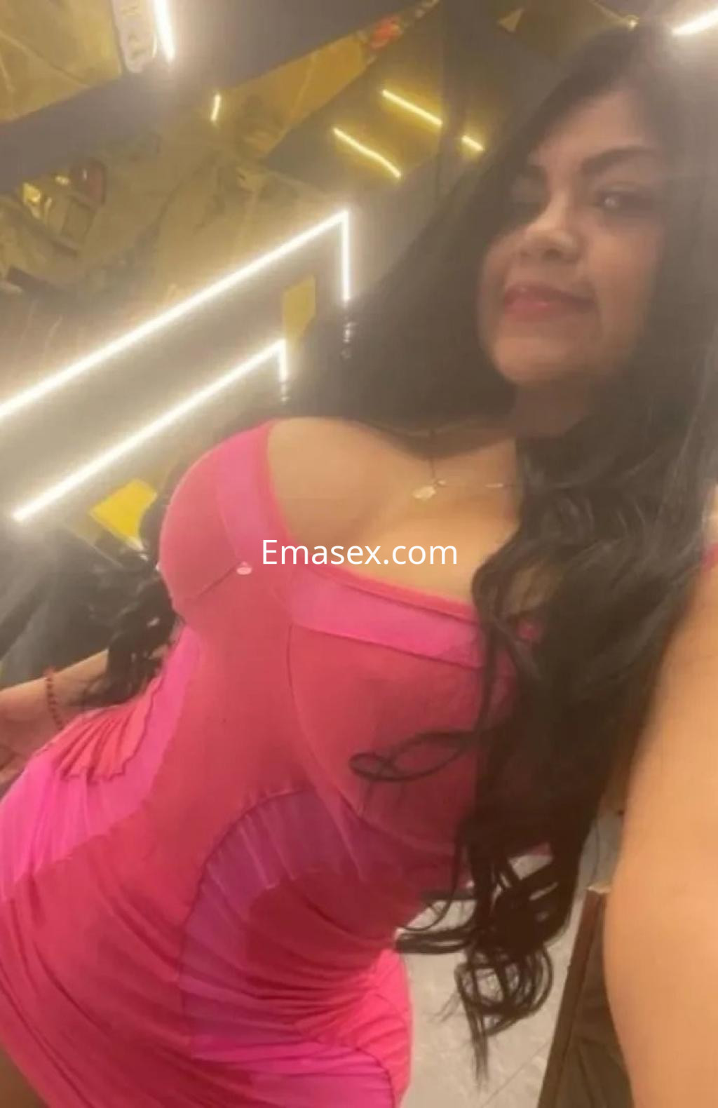 Puta posando con un vestido rosa ajustado, cabello largo y ondulado, en un ambiente iluminado en Vigo.