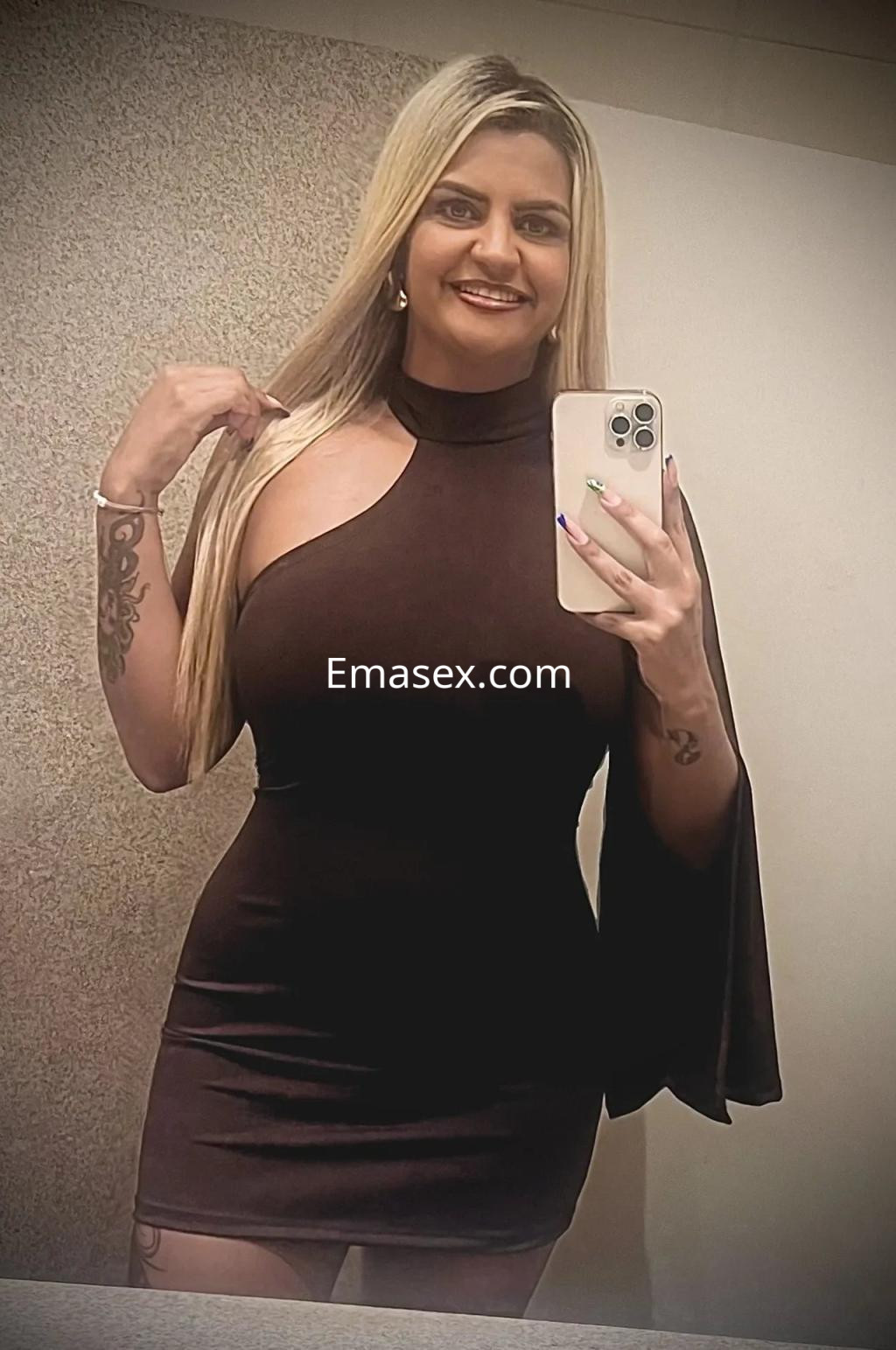 Escort en Vigo posando con un vestido negro ajustado, de manga larga y escote, mientras sonríe y se toca el cabello.