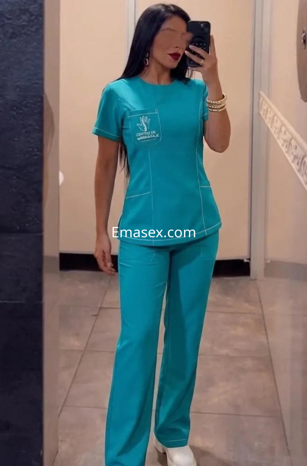 Escort en Vigo viste un uniforme azul claro con pantalones y camiseta, posando frente a un espejo.