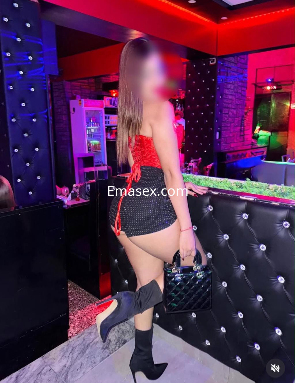 La puta viste un top rojo y una minifalda negra mientras sostiene un bolso, en un bar de Santander.