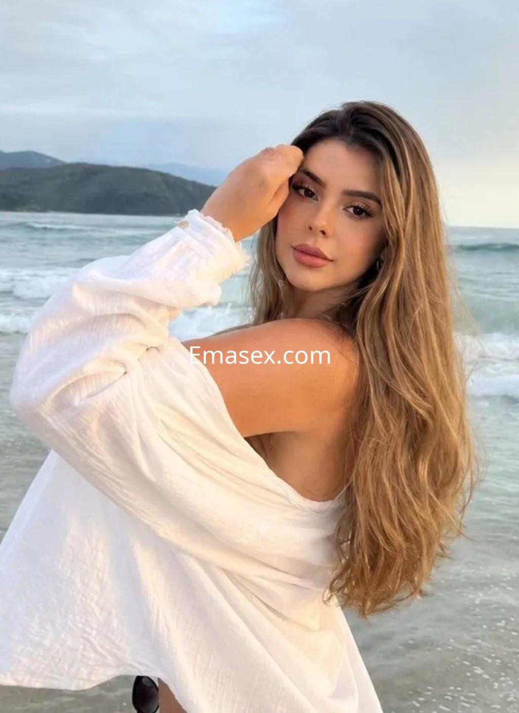 La puta luce una blusa blanca y tiene el cabello largo y suelto, posando en la playa de Córdoba.