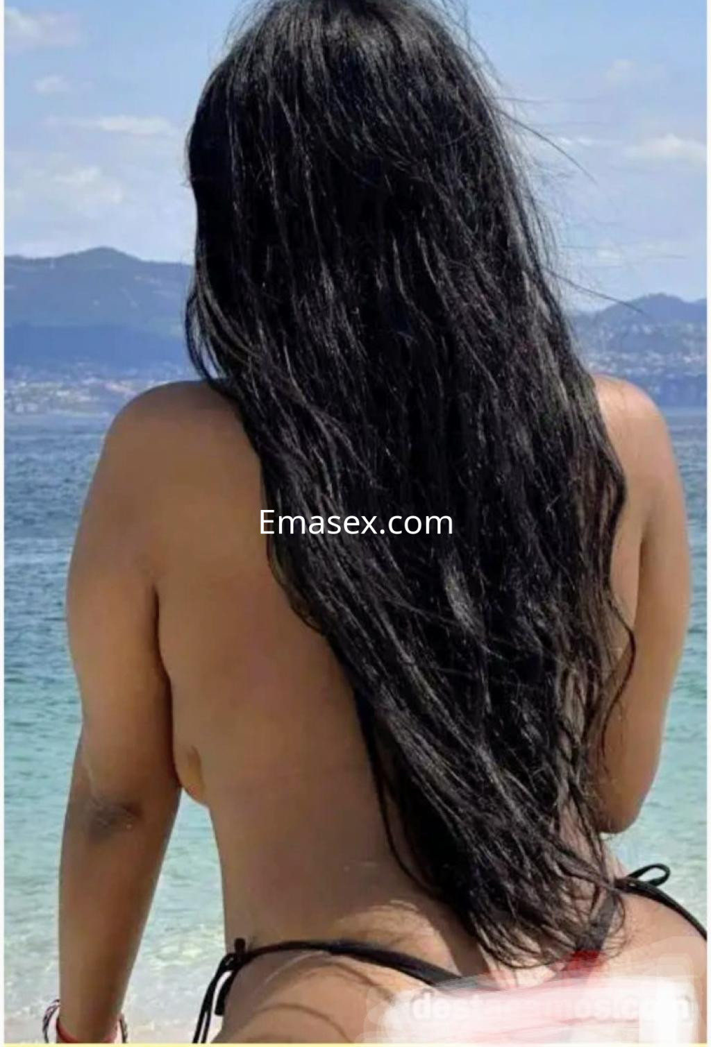 Escort de cabello largo y oscuro, de espaldas, en la playa con un paisaje de mar en Santiago.