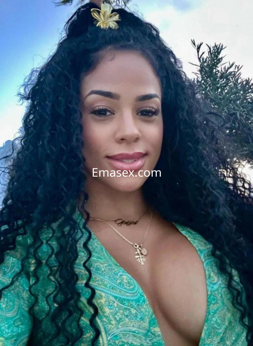 Escort en Almería con cabello rizado y largo, vistiendo un top verde, sonríe en un entorno natural.