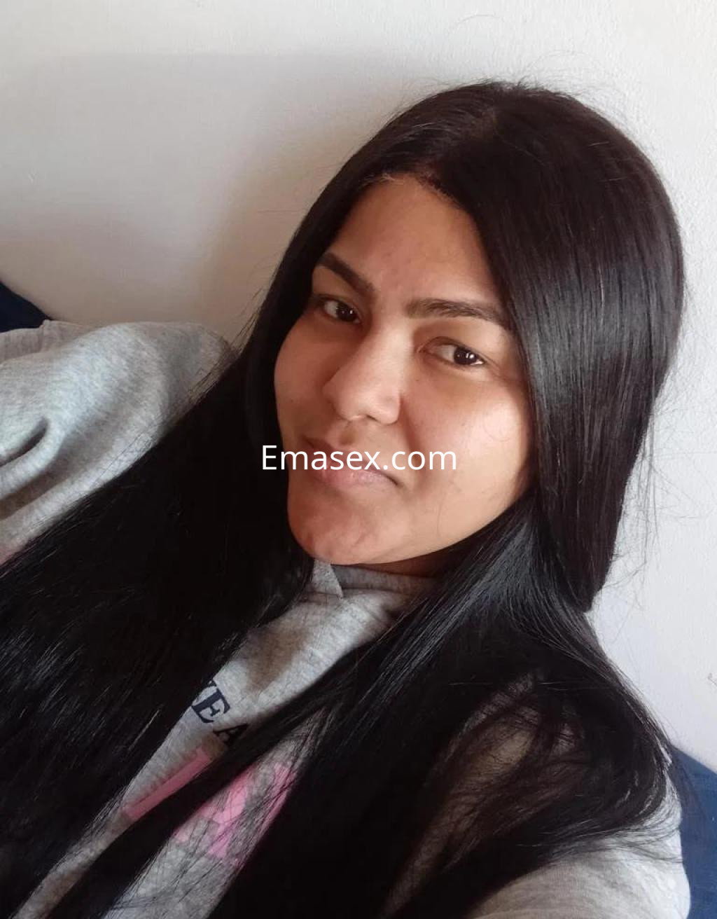 Escort en Barcelona con cabello largo y lacio, viste una sudadera gris y sonríe en un entorno casual.