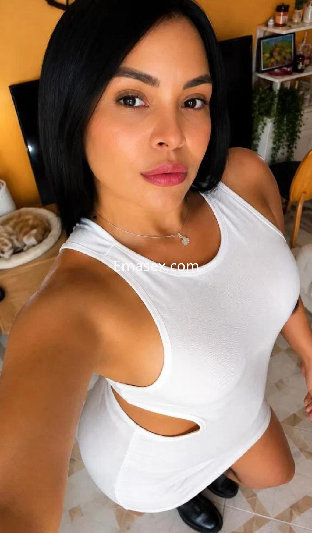 Escort en Coruña con cabello lacio y oscuro, vistiendo un vestido blanco ajustado y posando en un ambiente interior.