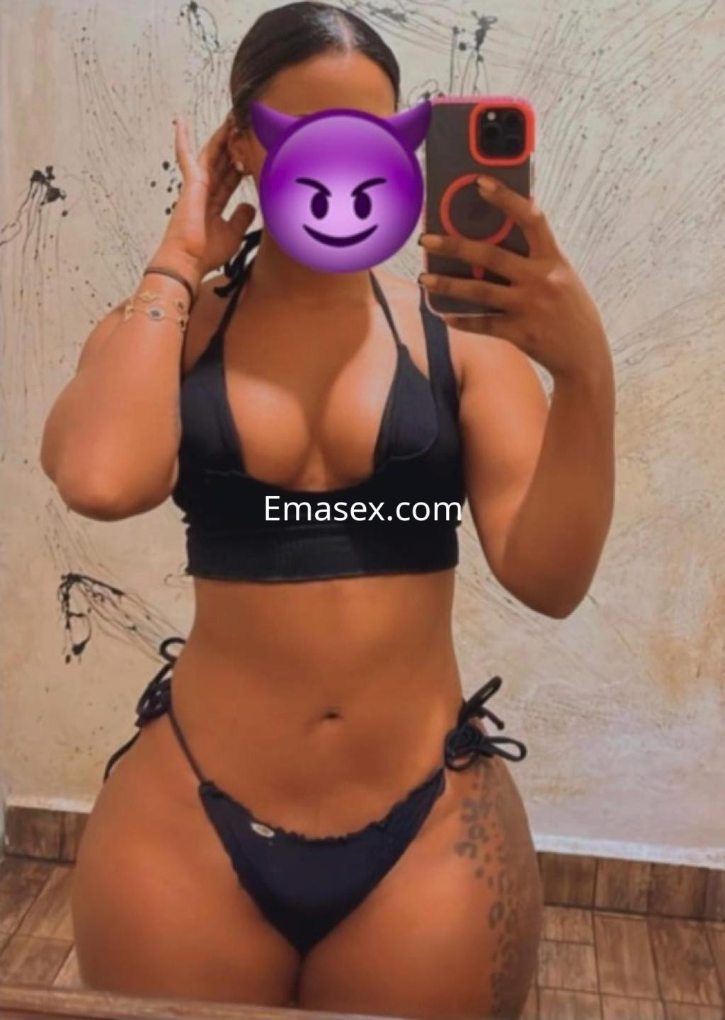 Escort en Santiago posando con un bikini negro, mostrando una figura curvilínea frente a un espejo.