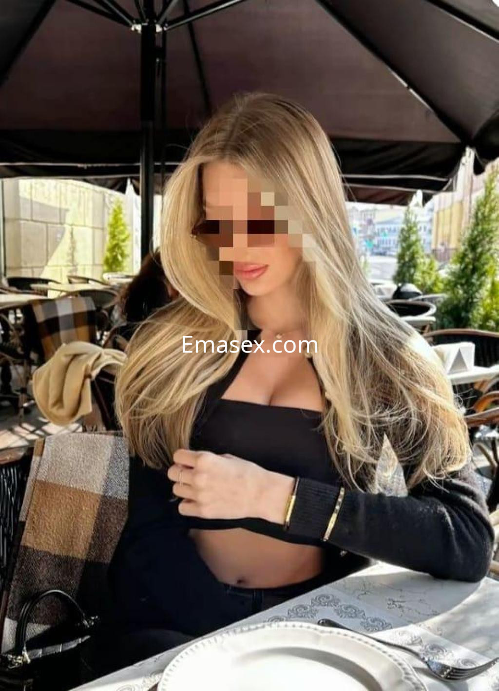 Puta rubia con cabello largo y lacio, viste un top negro y se encuentra sentada en una terraza en Huelva.