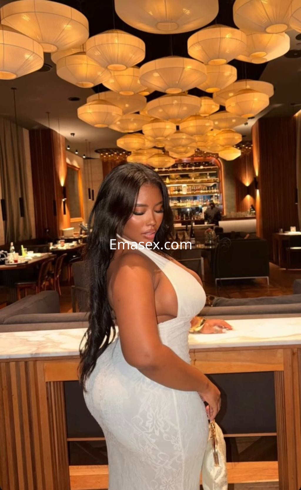 La escort posando con un vestido blanco ajustado en un elegante restaurante de Lugo, con cabello largo y oscuro.
