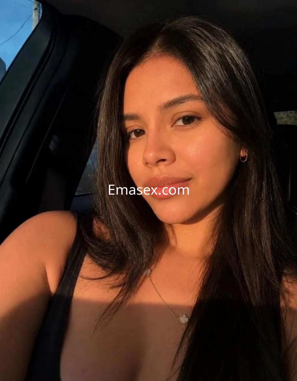 Escort en Madrid con cabello largo y oscuro, sonriendo suavemente en un entorno de automóviles.