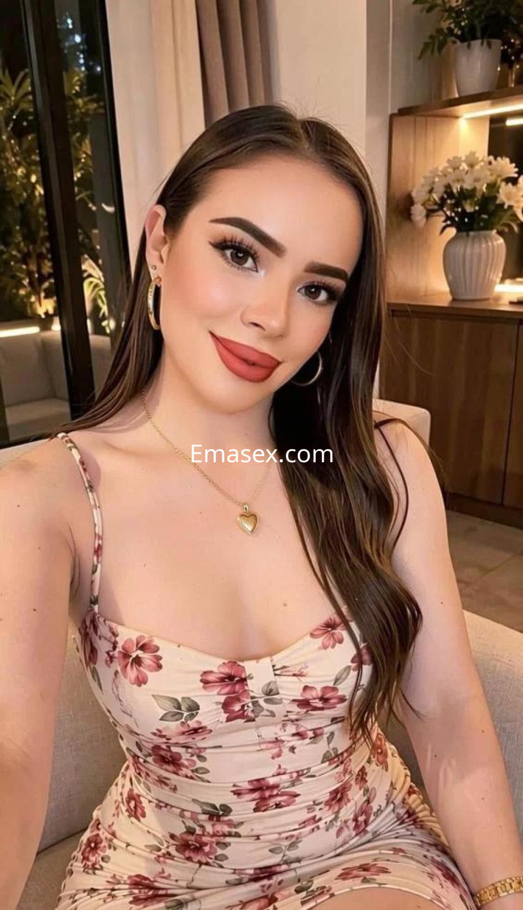 Puta en Madrid con cabello largo y ondulado, lleva un vestido floral ajustado y sonríe en un ambiente elegante.