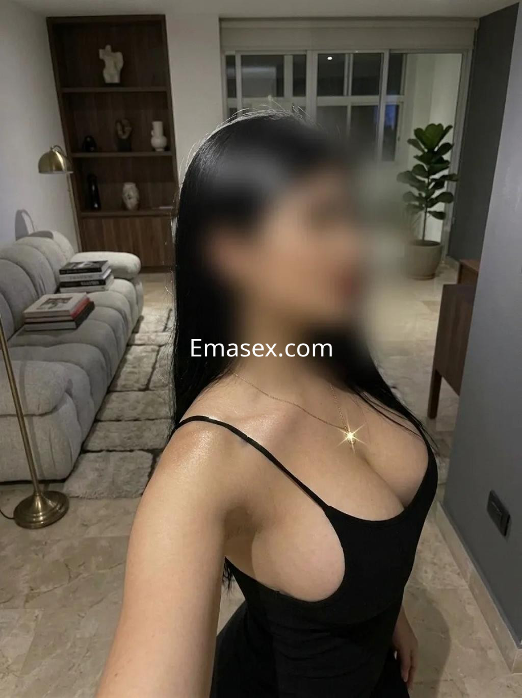 Escort en Madrid con cabello largo y lacio, luciendo un vestido negro ajustado en un entorno moderno y acogedor.