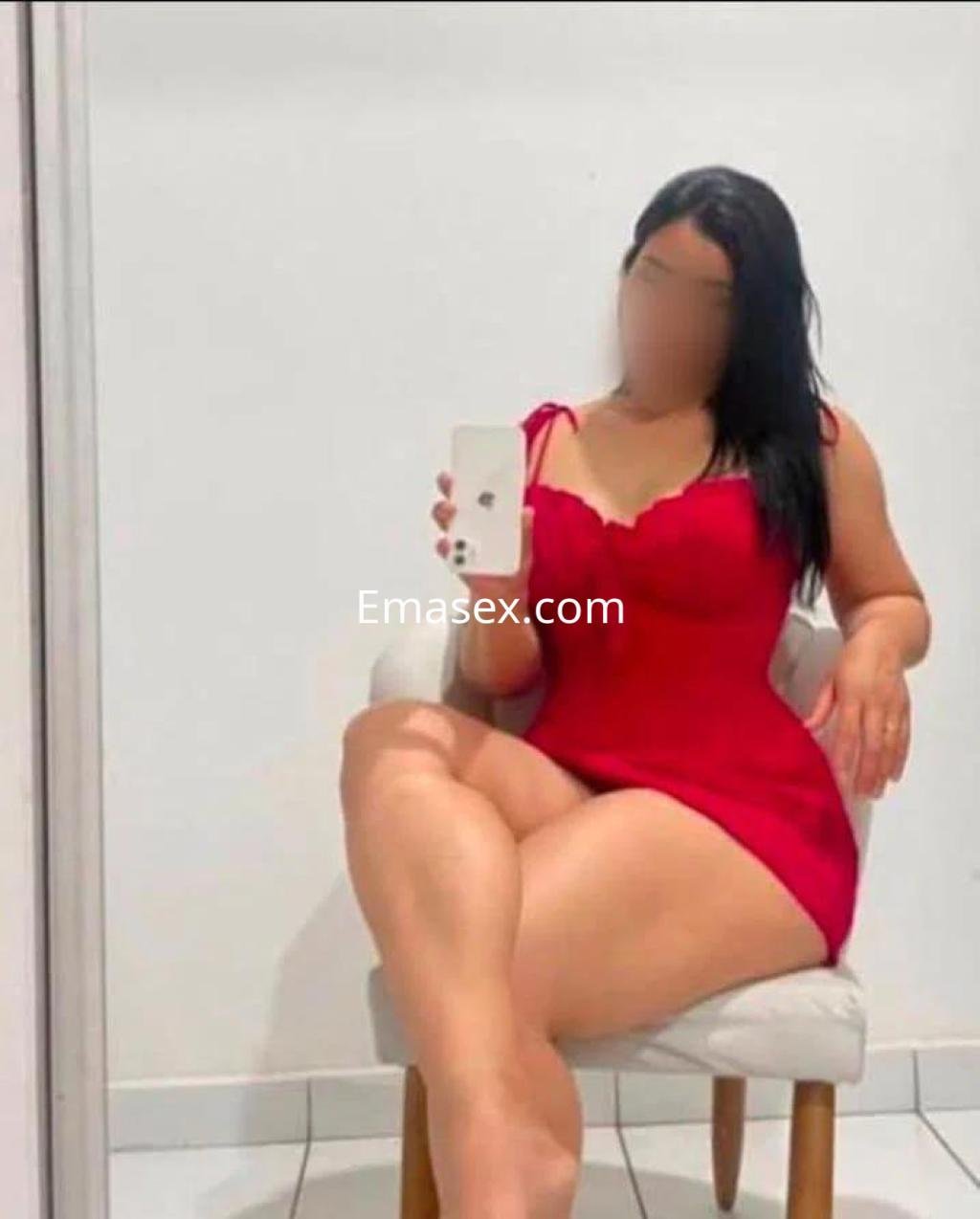 Escort en Sevilla posando sentada en una silla con un ajustado vestido rojo, mostrando una actitud relajada.