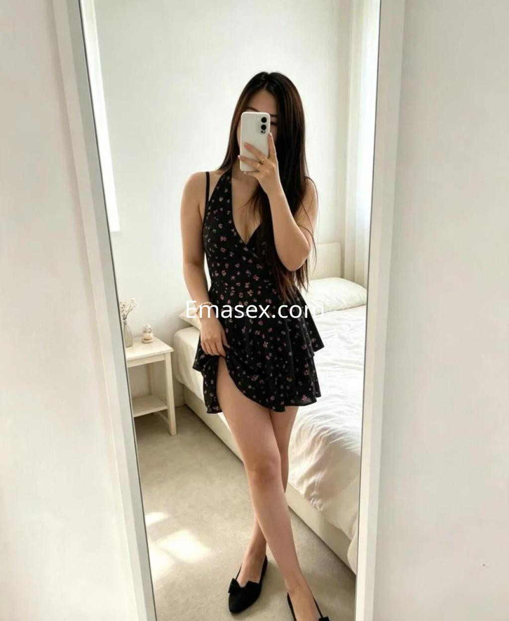 Puta en Sevilla, posando frente al espejo con un vestido corto negro con estampado floral y tacones.