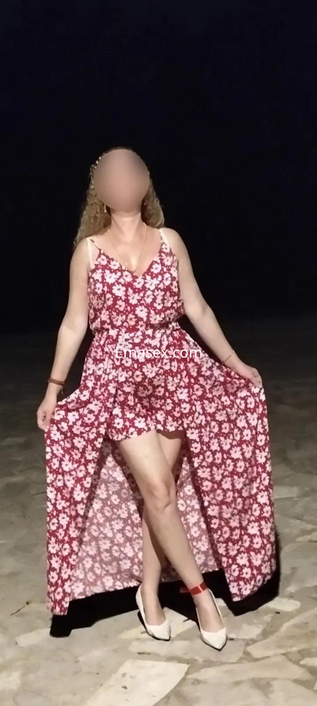 Escort en Valencia luciendo un vestido floral de tirantes con falda larga y sandalias, posando al aire libre.