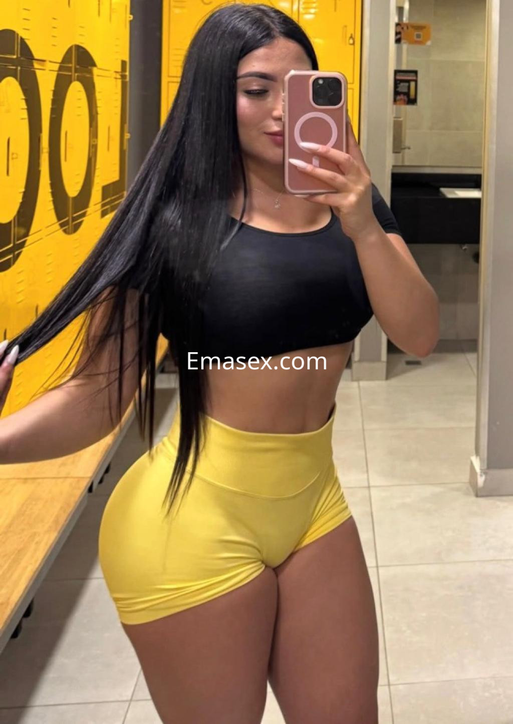 Puta con cabello largo y lacio, vestida con top negro y shorts amarillos, posando en un vestuario en Bilbao.