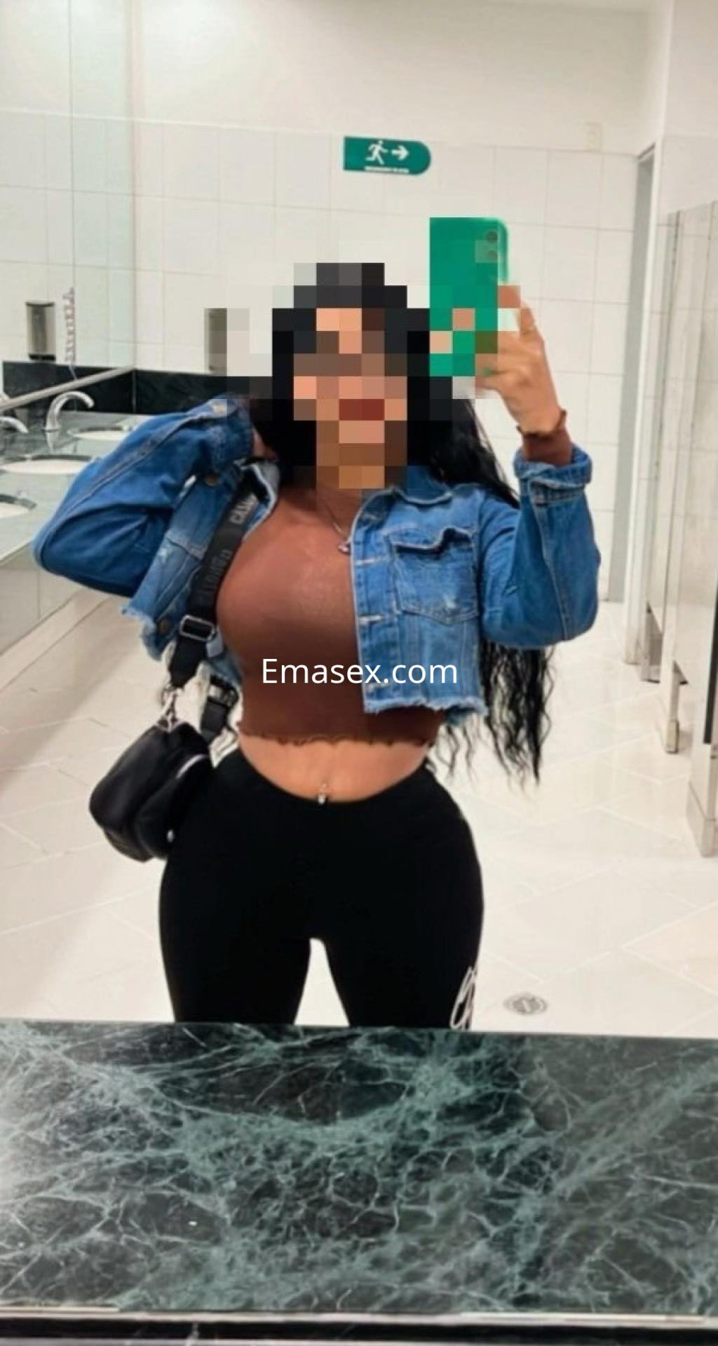 Puta en Málaga, con cabello largo y oscuro, lleva un top marrón y jeans ajustados, posando frente al espejo.