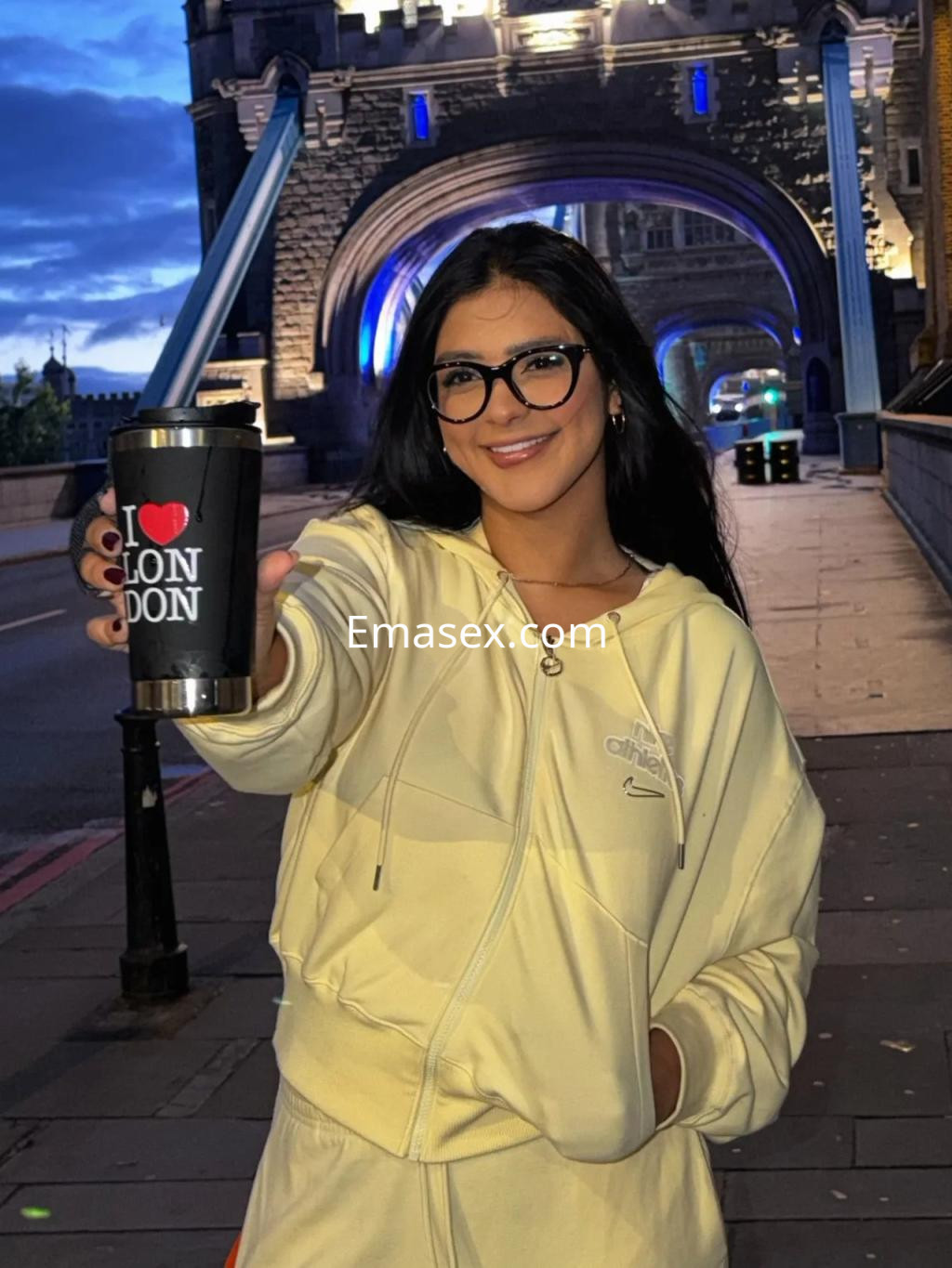 La puta luce un conjunto deportivo amarillo y gafas, posando sonriente con un vaso en la Coruña.