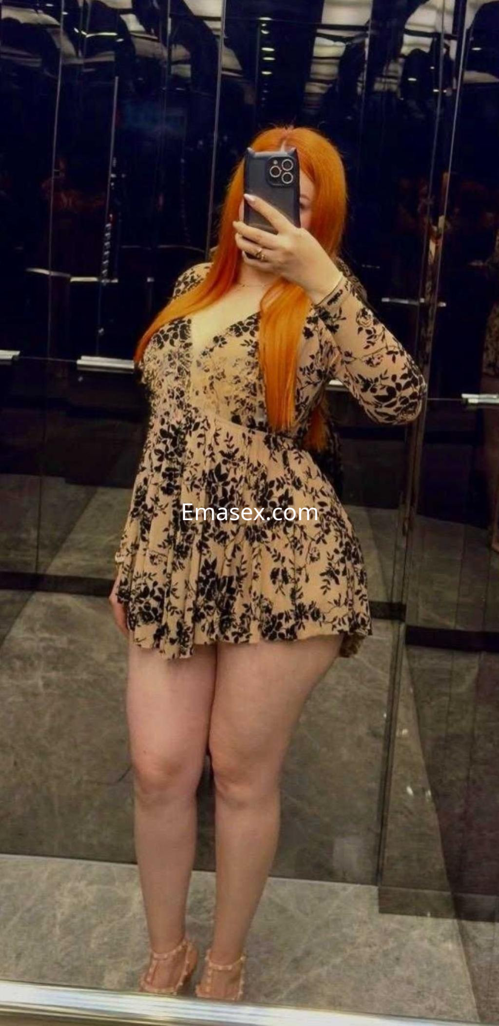 Escort en Burgos, con vestido claro de flores y cabello largo, posando frente a un espejo en un ambiente elegante.