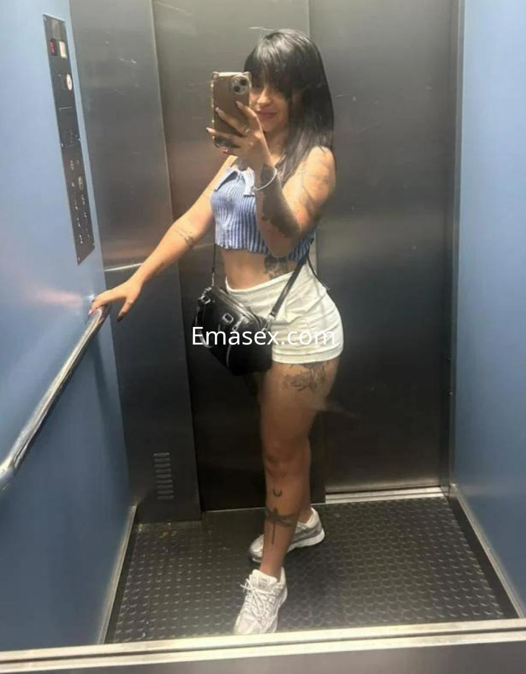 Puta con cabello largo y lacio, viste top a rayas y shorts claros, posando en un ascensor en Madrid.