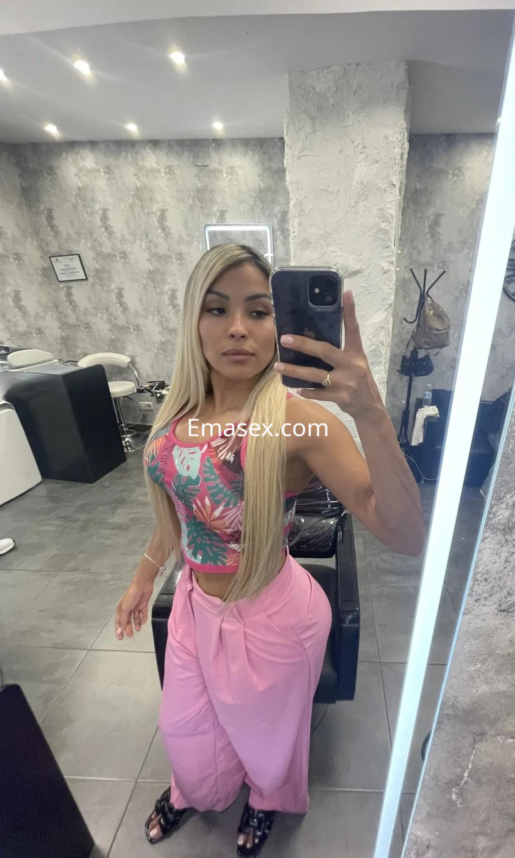 La puta en Córdoba muestra un top colorido y pantalones rosas mientras se toma un autorretrato en un salón.