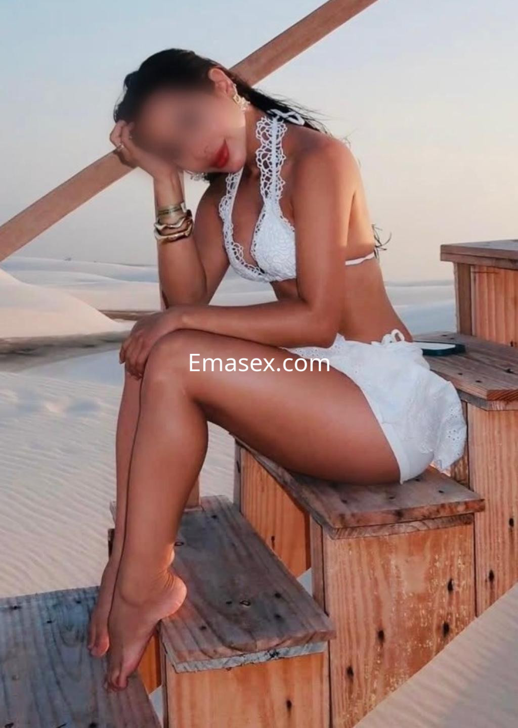 Puta posando en Pamplona, con un bikini blanco y short, sentada en una escalera de madera en un entorno arenoso.