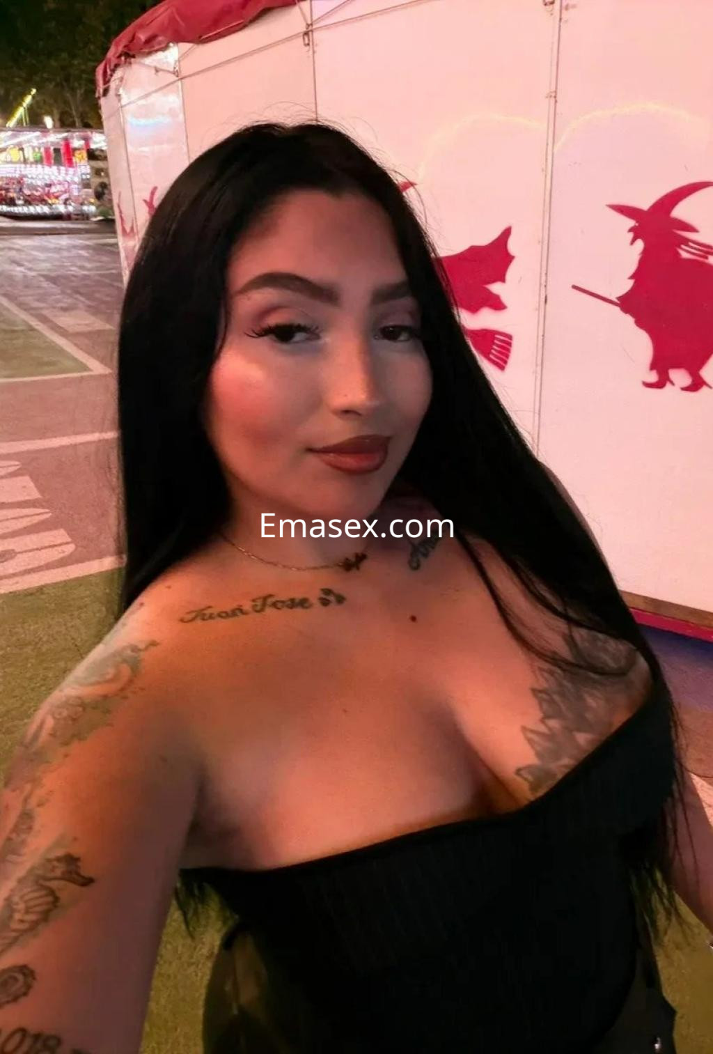 Escort en Barcelona con cabello largo y negro, luciendo un top ajustado y mostrando tatuajes en los brazos.